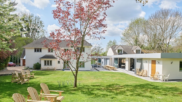 A modern house with a well-maintained lawn, outdoor seating, and a large tree with red leaves. - The Chase (Cheltenham)