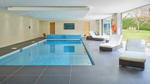 A modern indoor swimming pool with a clear view of the surrounding area, including a lounge area with seating and a view of the outdoors. - The Chase (Cheltenham)