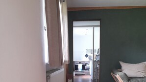 Un pasillo con un radiador, una alfombra blanca y un suelo de madera que conduce a una habitación con una cama y una mesita de noche.