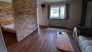 Una habitación con pared de madera, una cama, una ventana con cortinas, un radiador y un sofá.