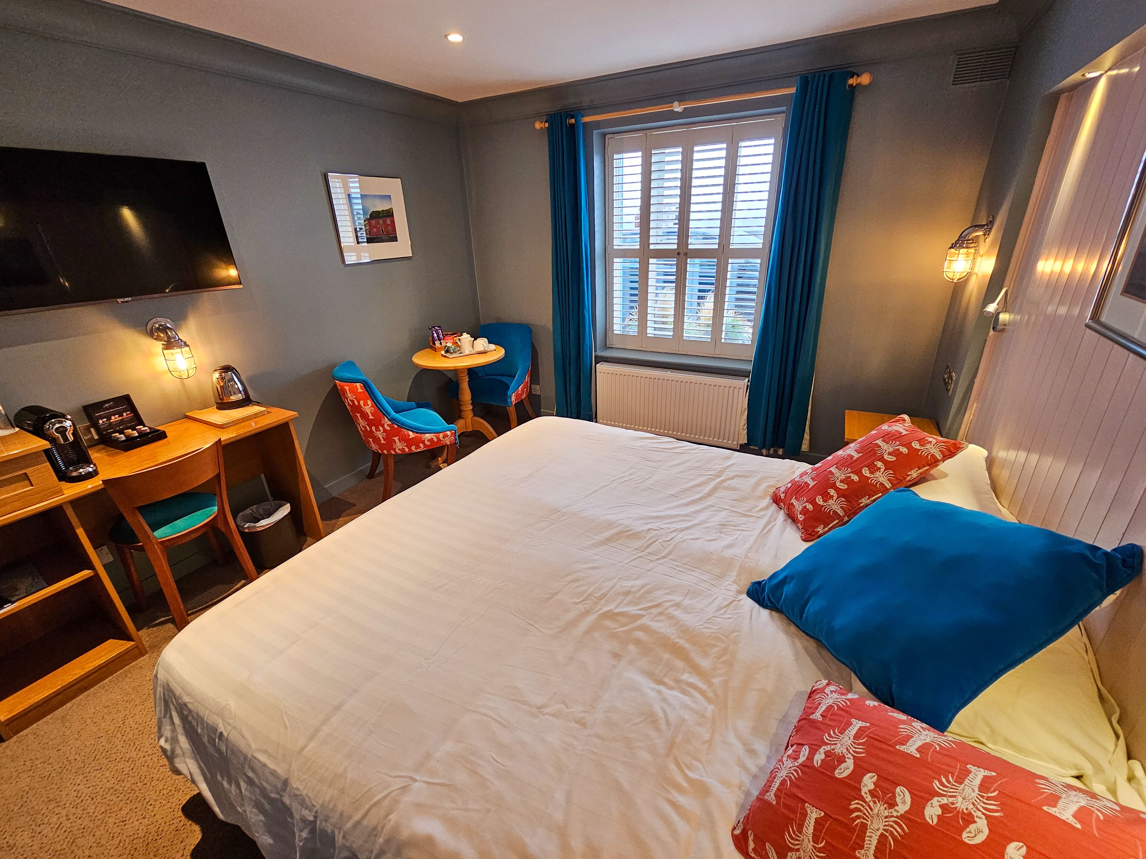 A hotel room with a large bed, a desk with a chair, a flat-screen TV, and a window with curtains.