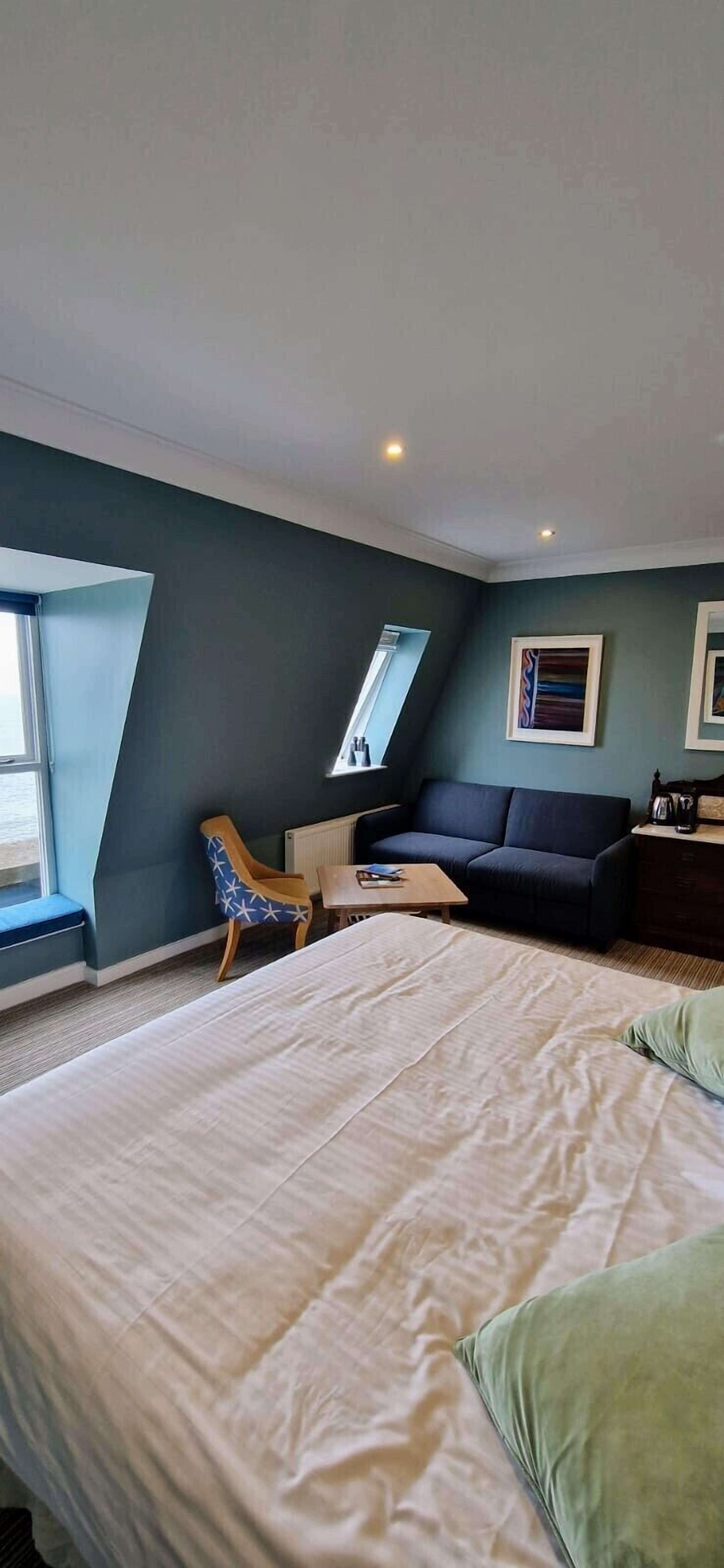 A bedroom with a large bed, a sofa, a chair, a small table, and a radiator.