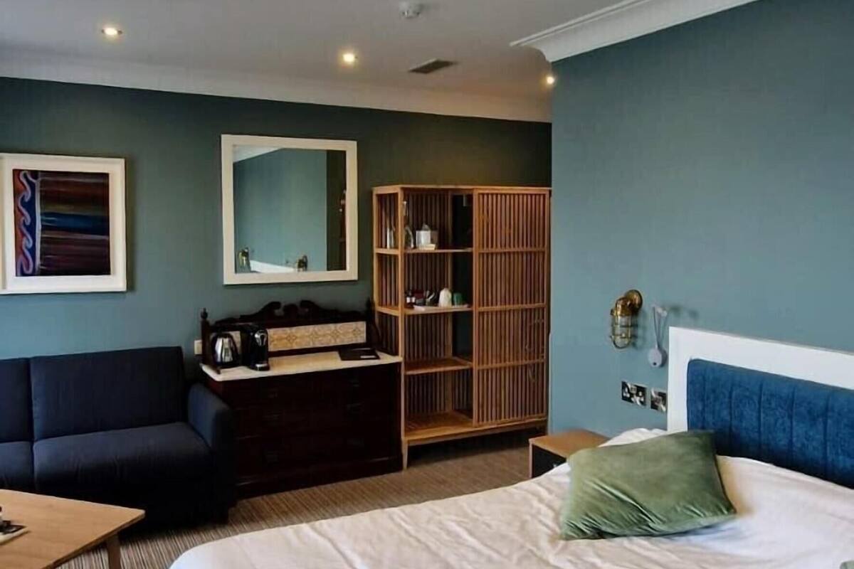A hotel room with a large bed, a sofa, a wooden wardrobe, a desk, and a mirror.