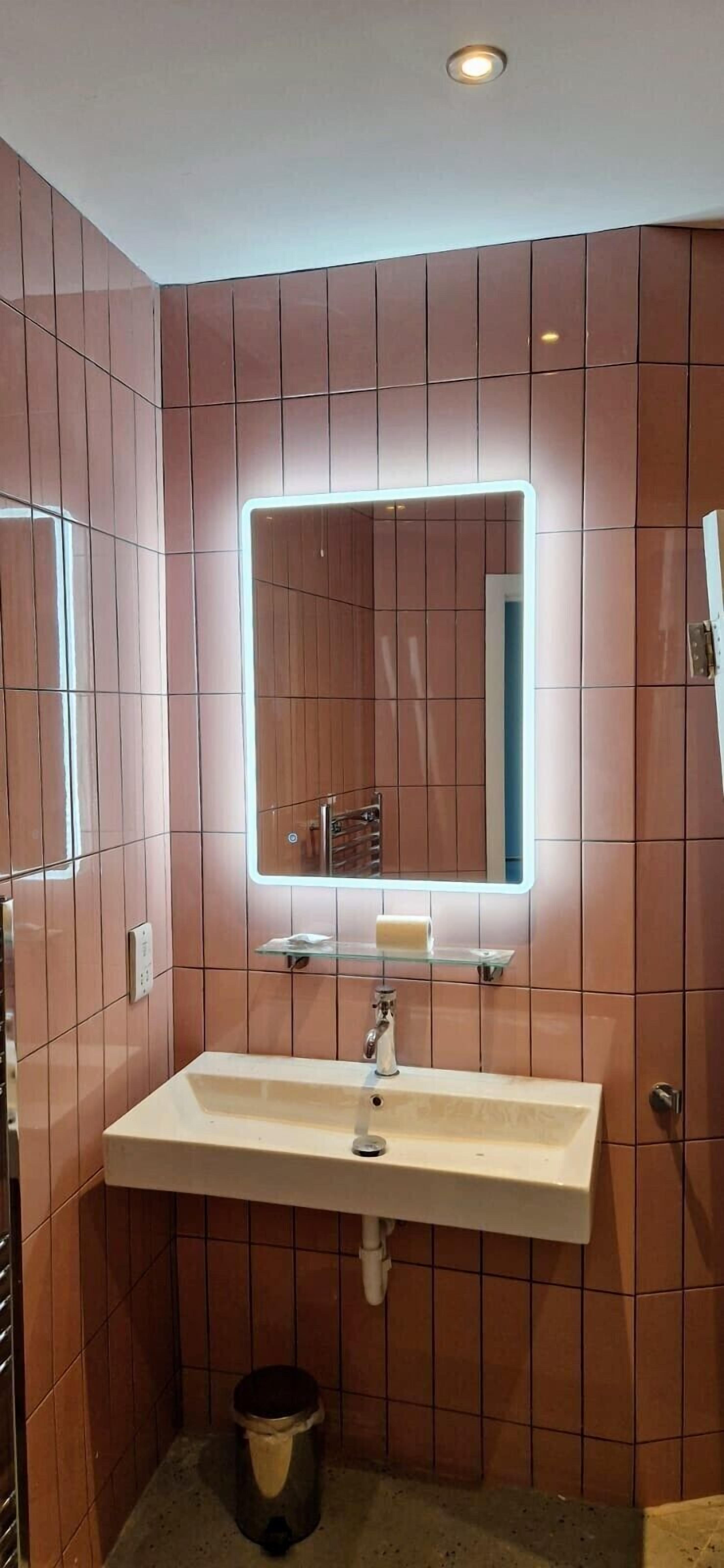Un baño con un lavamanos blanco, un espejo con luz y paredes de azulejos marrones.