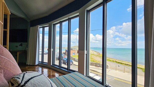 Une chambre dotée de grandes fenêtres donnant sur un port de plaisance et une plage.