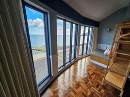 Quarto com grandes janelas com vista para um corpo de água, piso de madeira e um banco embutido com escada.