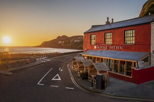 Um edifício costeiro chamado 'King Sitric', com fachada vermelha, grandes janelas e vista para o mar.