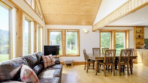 A spacious living area with a leather sofa, wooden dining table, and large windows.