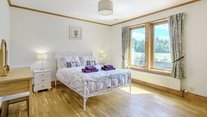 A bedroom with a bed, bedside tables, a desk, a window with curtains, and a ceiling light fixture.