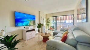 Un salon moderne doté d’un téléviseur à écran plat, d’un canapé gris, d’une table basse et d’un coin repas avec des chaises et une table.