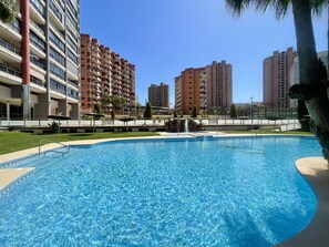 A swimming pool with a tiled edge, surrounded by a low fence, with tall residential buildings in the background. - TORRE DOSCALAS PONIENTE R114 (Benidorm)