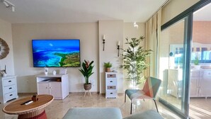 Un salon moderne doté d’un téléviseur à écran plat, d’un coin repas avec une table et des chaises, et d’une grande fenêtre offrant une vue sur l’extérieur.