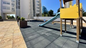 A playground with a slide and swings, surrounded by a paved area and tall buildings in the background. - MIRAGOLF PONIENTE DREAM R118 (Benidorm)