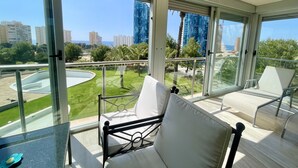 A balcony with a glass railing, white cushioned chairs, and a view of a cityscape and greenery. - MIRAGOLF PONIENTE DREAM R118 (Benidorm)
