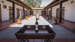 Une cour intérieure avec une table centrale sur laquelle sont posés une bouteille et des verres, entourée de plantes en pot et d’une structure en forme de pergola.