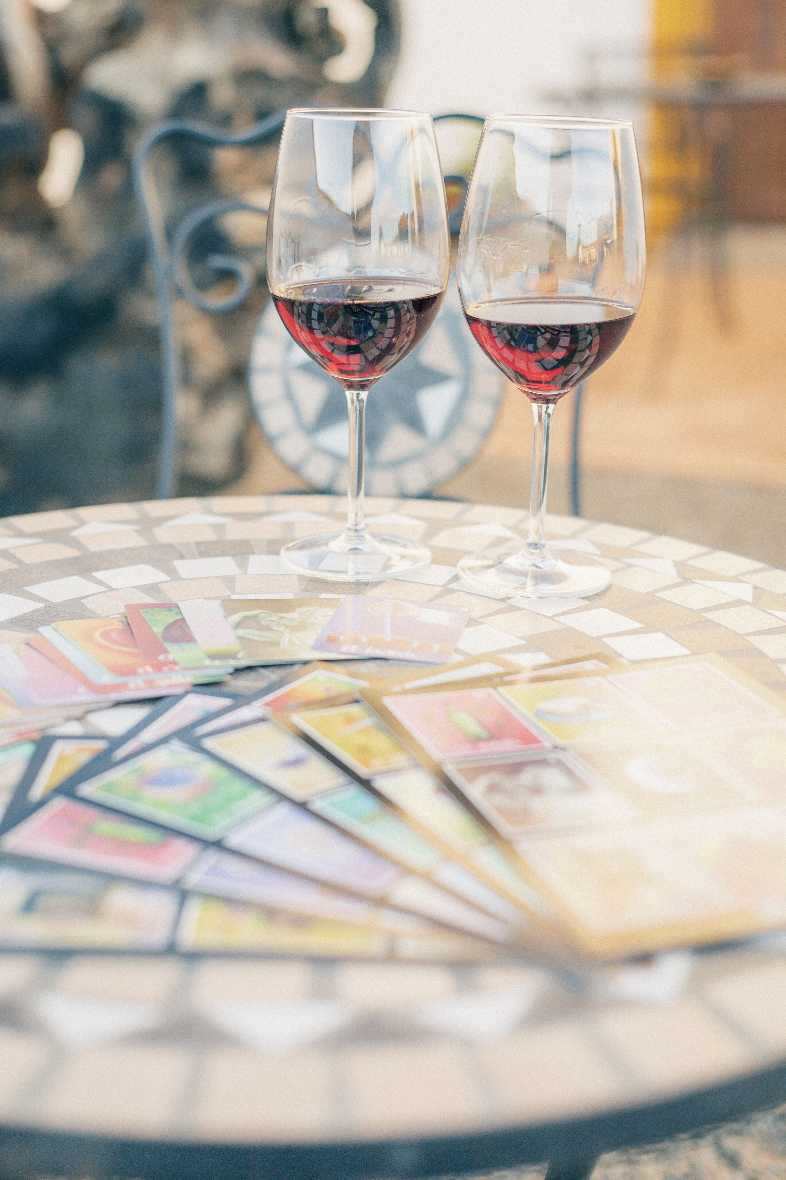 Deux verres à vin sur une table à motifs de mosaïque, avec des jeux de cartes à proximité.
