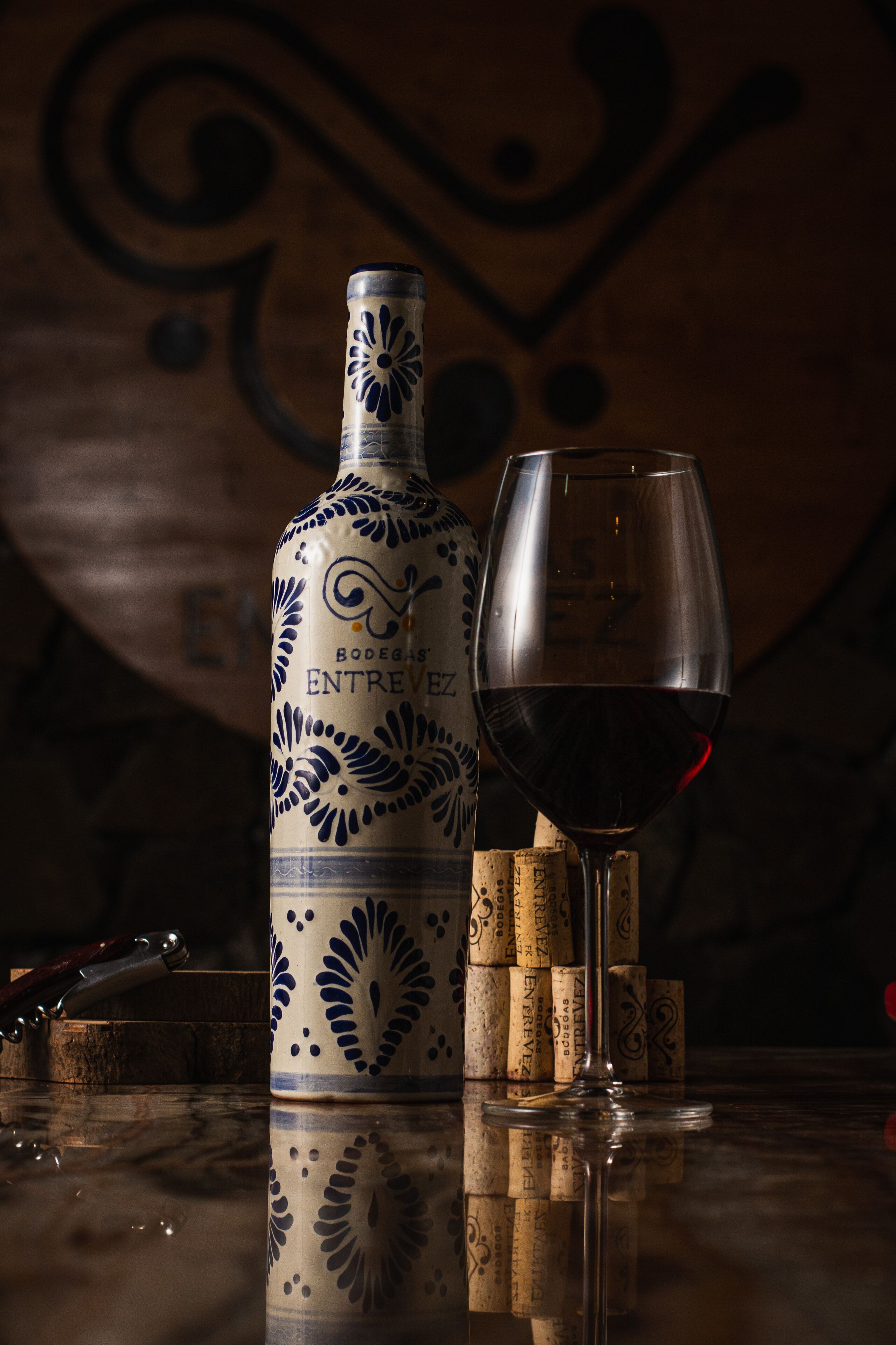 Eine Flasche Entrevez Wein von Bodega, ein Weinglas und mehrere Weinkorken auf einer spiegelnden Oberfläche.