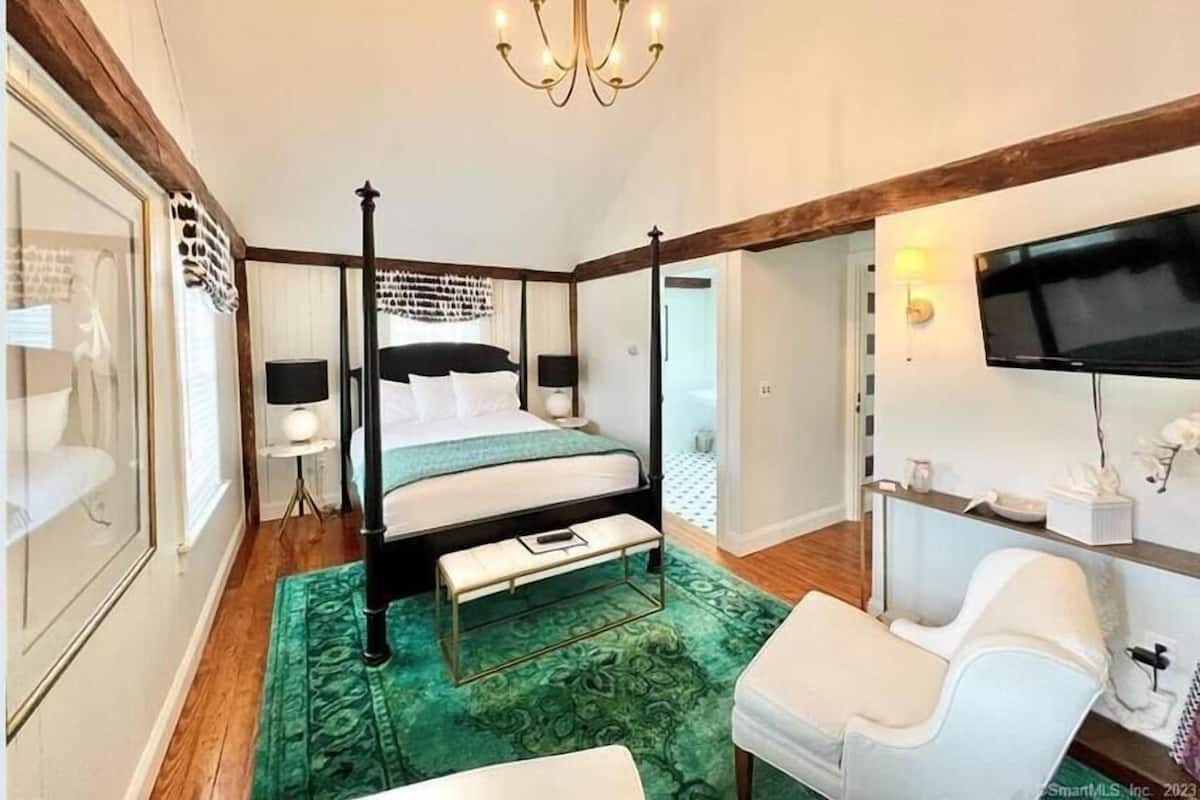 Un lit à baldaquin, une moquette verte, un fauteuil blanc, un téléviseur fixé au mur et un lustre.