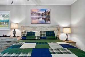 Ein Schlafzimmer mit einem großen Bett, zwei Nachttischlampen, einem hölzernen Kopfteil, einem Gemälde einer Seenlandschaft und einem Fenster mit Jalousien.
