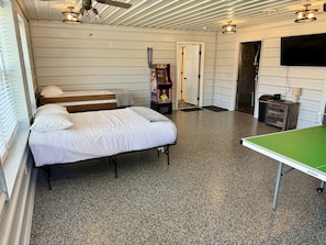 A room with a bed, a ping pong table, a door, and a wall-mounted TV.