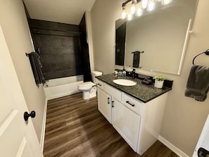 A bathroom with a white toilet, a sink with a granite countertop, a large mirror, and a shower area.
