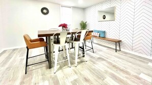 Un comedor con una mesa de madera, cuatro sillas, un banco, un espejo y un reloj en la pared.