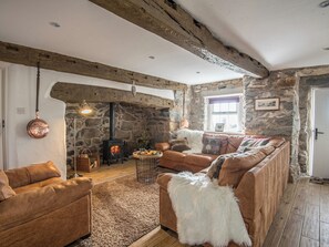A rustic living room with a stone wall, a fireplace, leather sofas, and a wooden ceiling. - 3 bedroom accommodation in Llaniestyn, near Abersoch (Llaniestyn, near Abersoch)