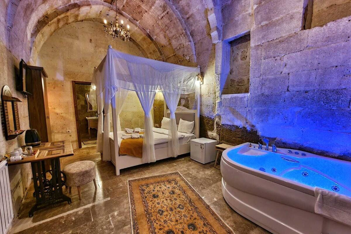 A room with a bed under a canopy, a sitting area with a table and chairs, a large bathtub, and stone walls.
