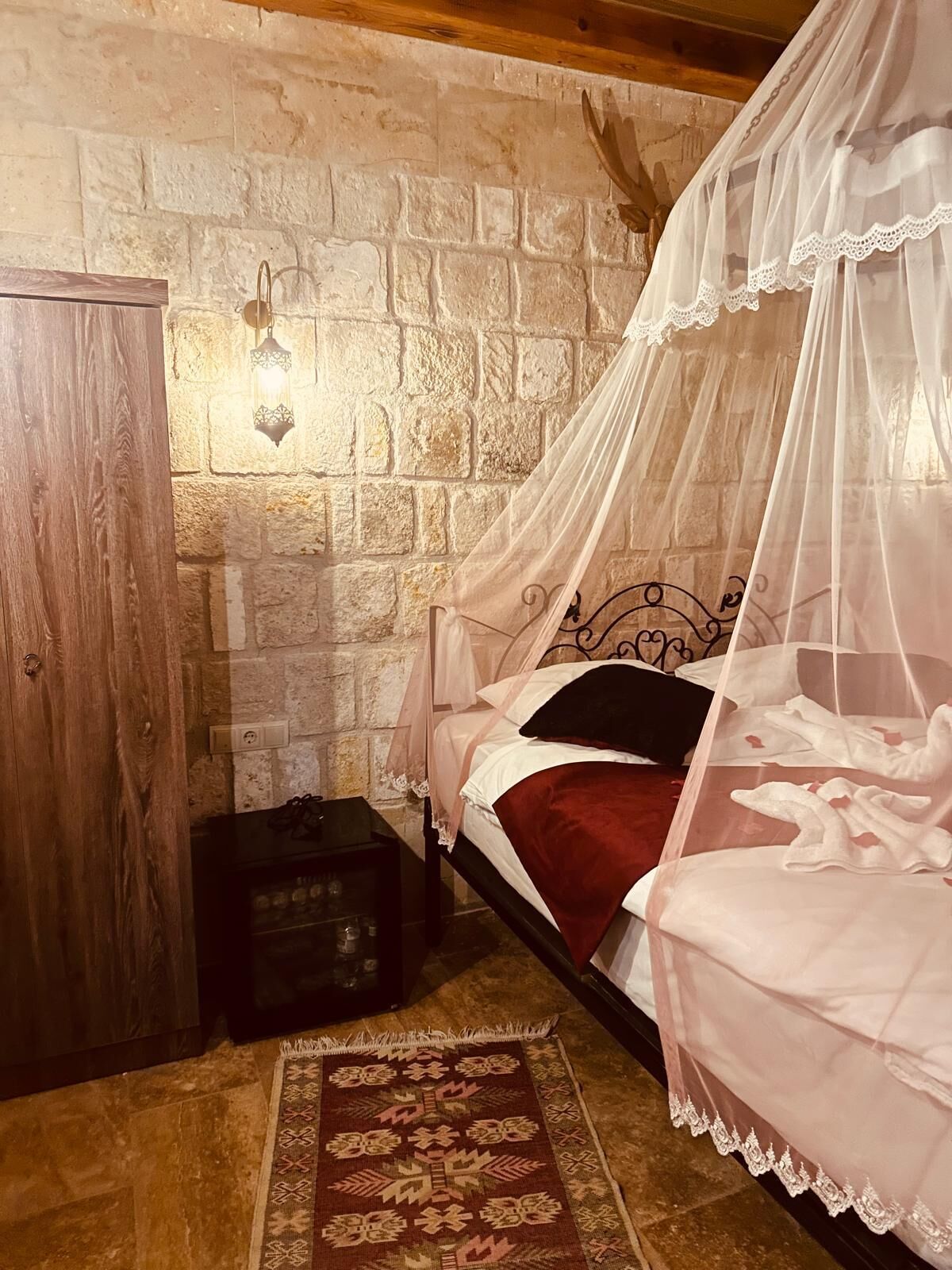 Un dormitorio con pared de piedra, cama con dosel, mesita de noche y alfombra estampada.