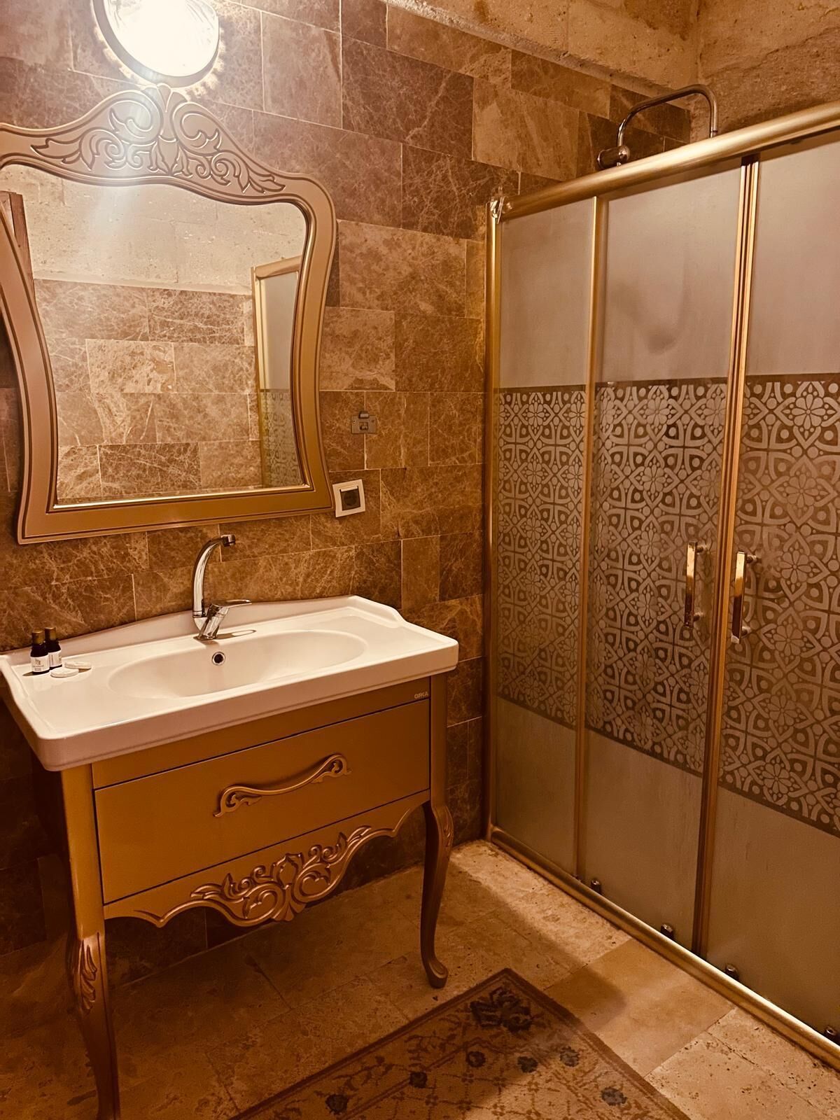 Een badkamer met een marmeren wastafel, een spiegel, een douche met betegelde wanden en een decoratief vloerkleed.