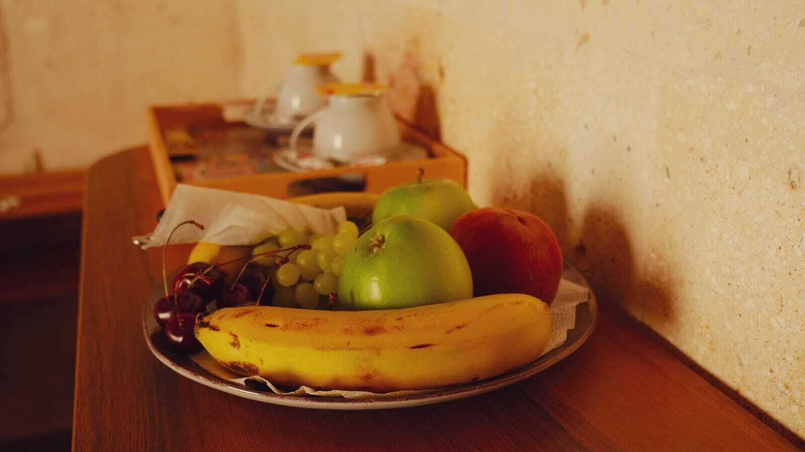 A plate of fruit on a wooden table with a white wall in the background.