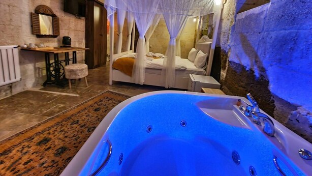 A room with a large bathtub, a bed with a canopy, a small table with a mirror, and a radiator. - Lavinia Cappadocia (Ürgüp)