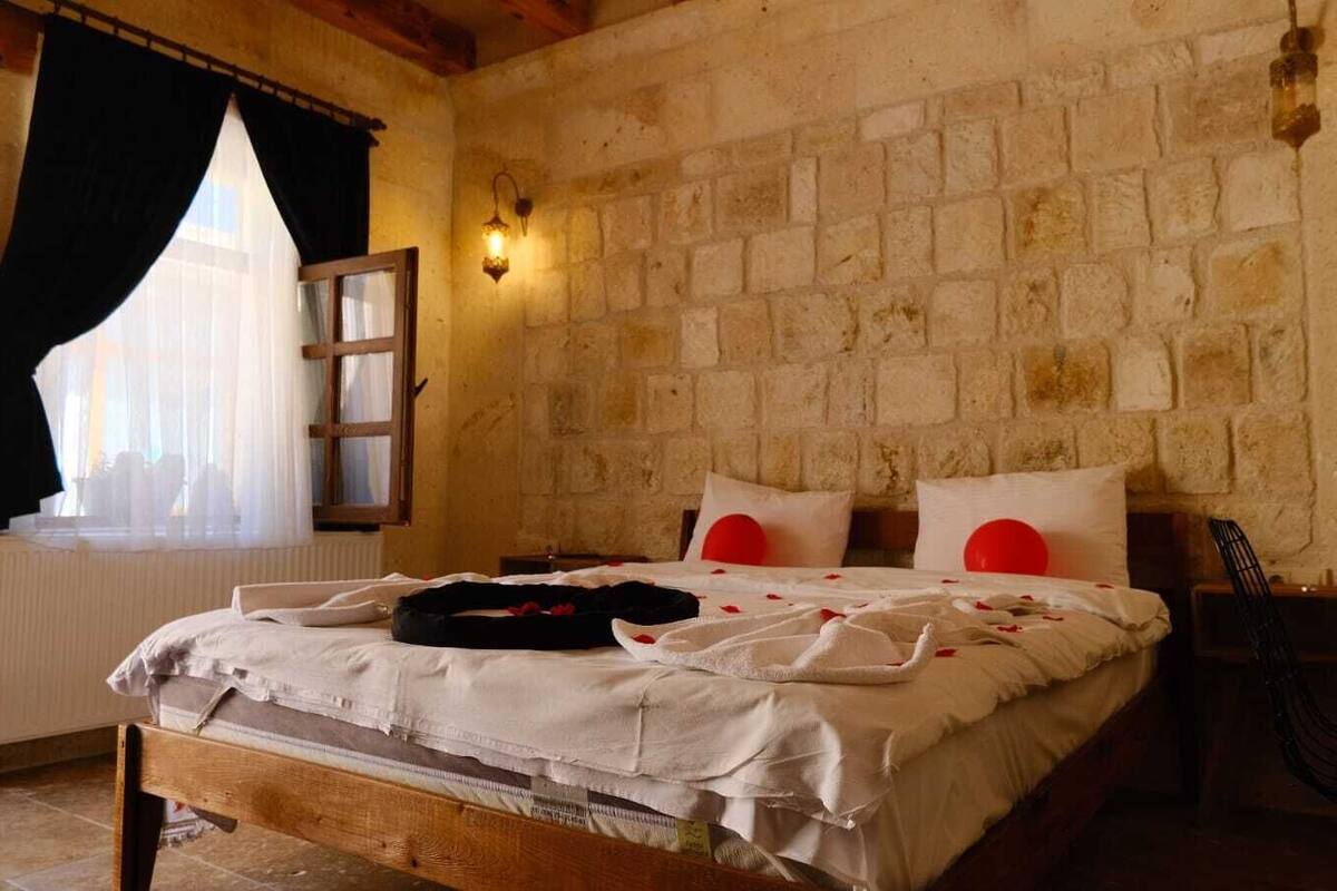A rustic bedroom with a stone wall, a wooden bed frame, and a window with sheer curtains.