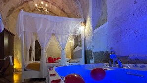 A room with a large bathtub, a bed with a canopy, and a chandelier. - Lavinia Cappadocia (Ürgüp)