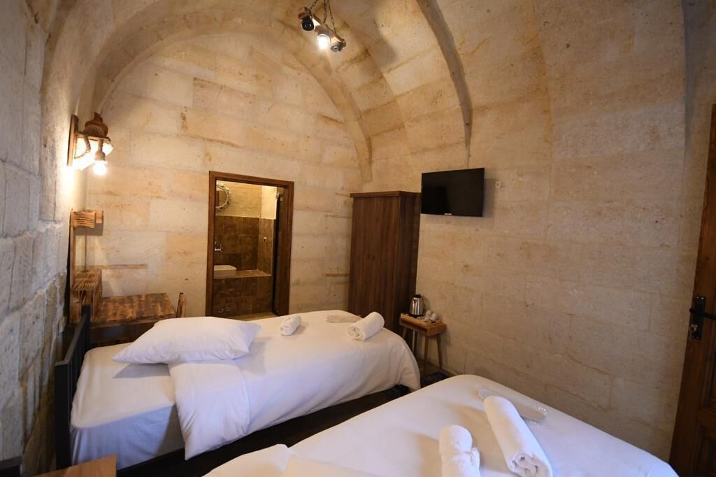A room with two beds, a wooden wardrobe, a flat-screen TV, and a stone wall.