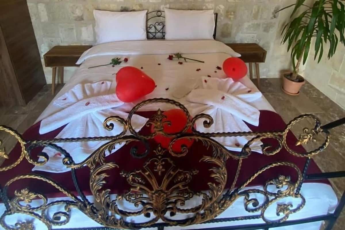 A bed with a decorative headboard, a stone wall with a deer head, and two wall-mounted lights.