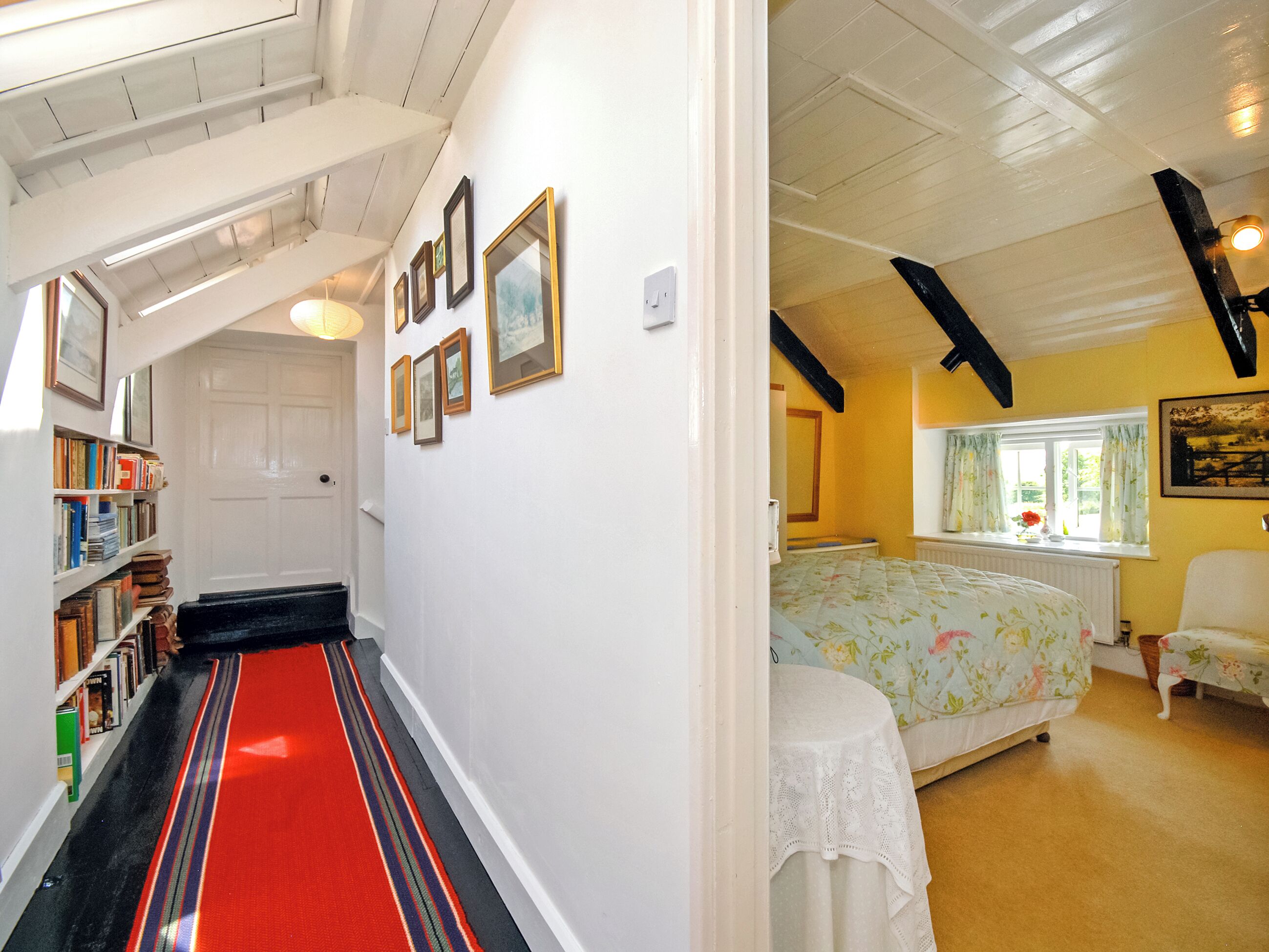 A hallway with a red carpet leading to a bedroom with a floral bedspread and a white table.