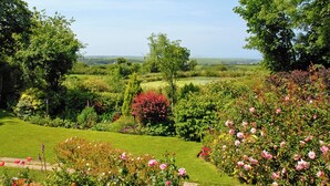 Un jardin luxuriant, avec une grande variété de fleurs et d’arbres, une pelouse bien entretenue et une vue sur la campagne.