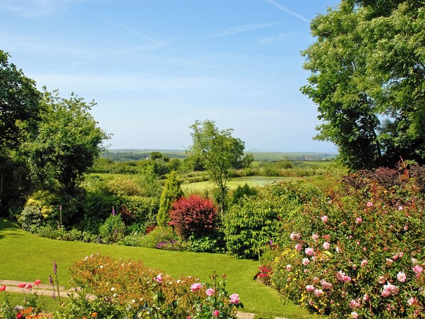 A lush garden with a variety of flowers and trees, a well-maintained lawn, and a view of the countryside.