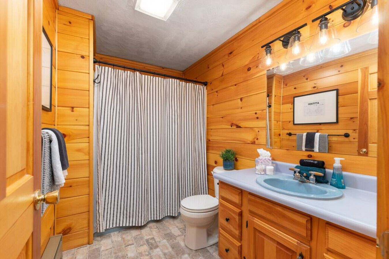 A wooden-paneled bathroom with a toilet, sink, and shower curtain.