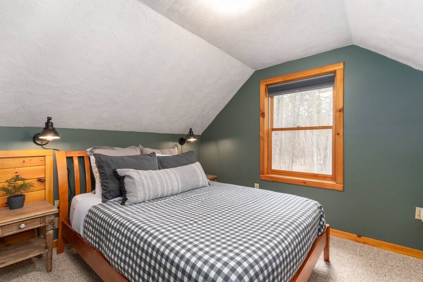 Une chambre à coucher avec un lit, deux lampes de chevet, une table de chevet, une fenêtre et une vue sur les arbres.