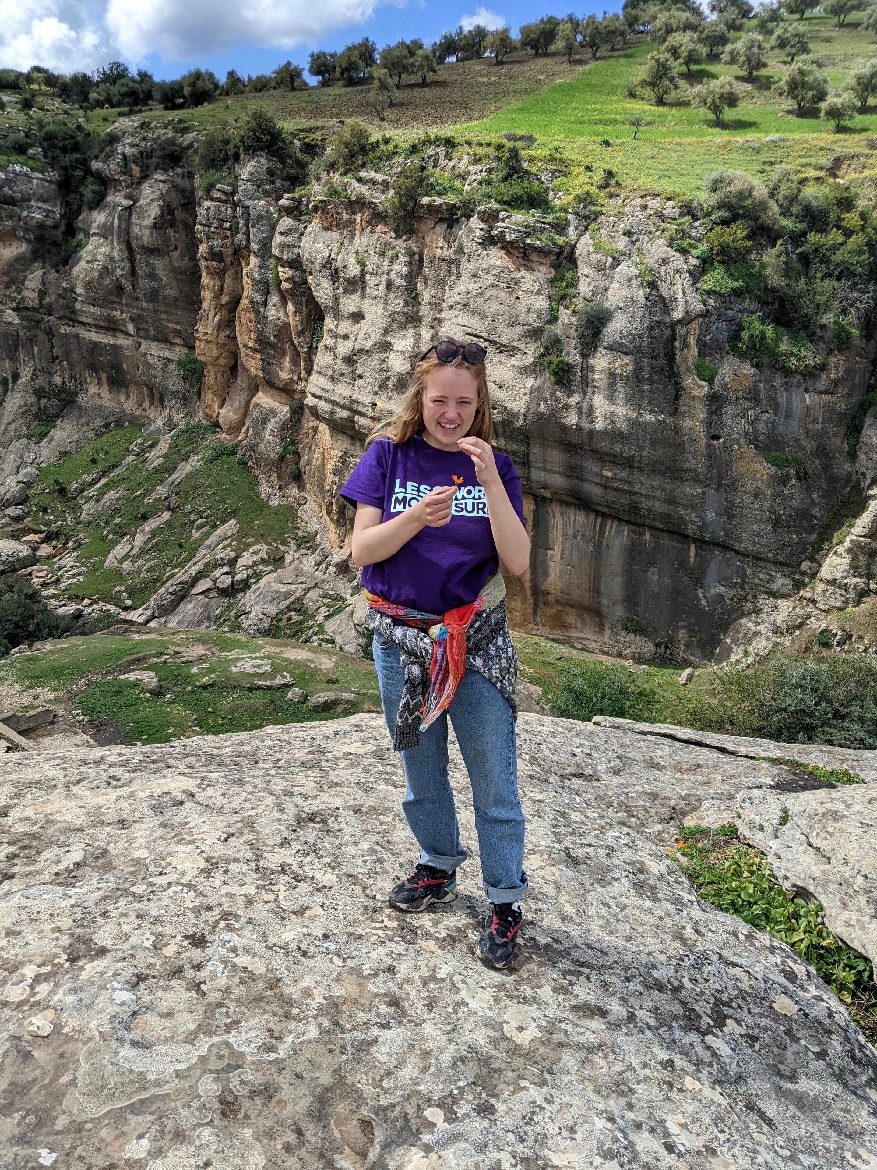 A person standing on a rocky outcrop with a mountainous landscape in the background.
