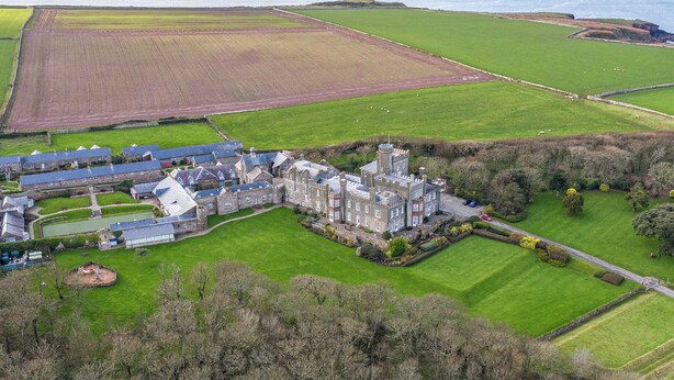 Un vaste domaine comprenant un bâtiment qui ressemble à un château, de vastes champs verdoyants et une vue sur la mer.