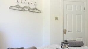 Un dormitorio ordenado con cama, perchero con perchas, una puerta y una bandeja con cruasanes y cafetera.