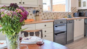 Una cocina con armarios blancos, encimera de madera, una mesa de comedor con un florero y una copa de vino.