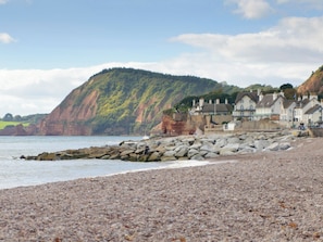 A coastal scene with a pebble beach, a rocky breakwater, and a row of traditional houses with steep roofs. - Seascape is a coastal holiday home situated in the seaside resort of Sidmouth. (Sidmouth)