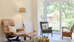 Una sala con sillones de cuero, una mesa con tazas y pasteles, una lámpara y vistas al verde exterior.