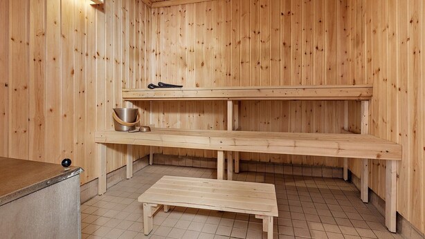 Un cuarto de sauna con paredes de madera, un banco, un estante con un balde y un par de pantuflas, y suelo de baldosas.