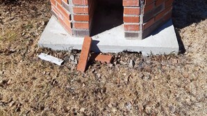 Una pequeña construcción de ladrillo con base de hormigón, posiblemente un cobertizo o un edificio pequeño, rodeado de hierba seca y hojas.