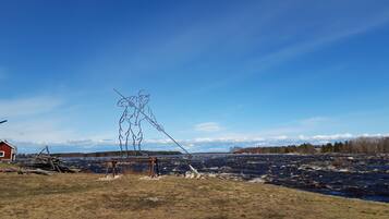 A rural landscape with a clear sky, a wooden sculpture, a red building, and a river.